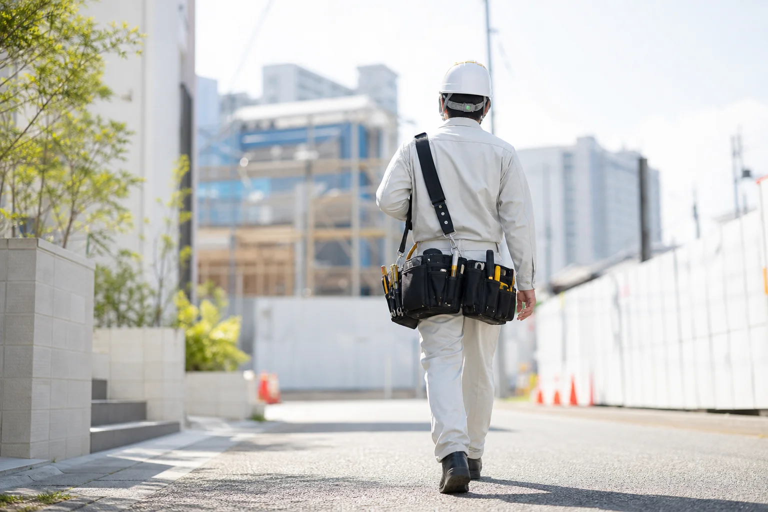 朝の光の中、工具袋を持って新しい現場へ向かう電気工事士の後ろ姿
